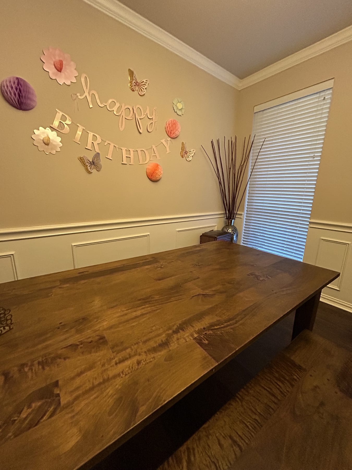 A long plank dining table with nobody at it, and a paper happy birthday banner still up on the wall behind